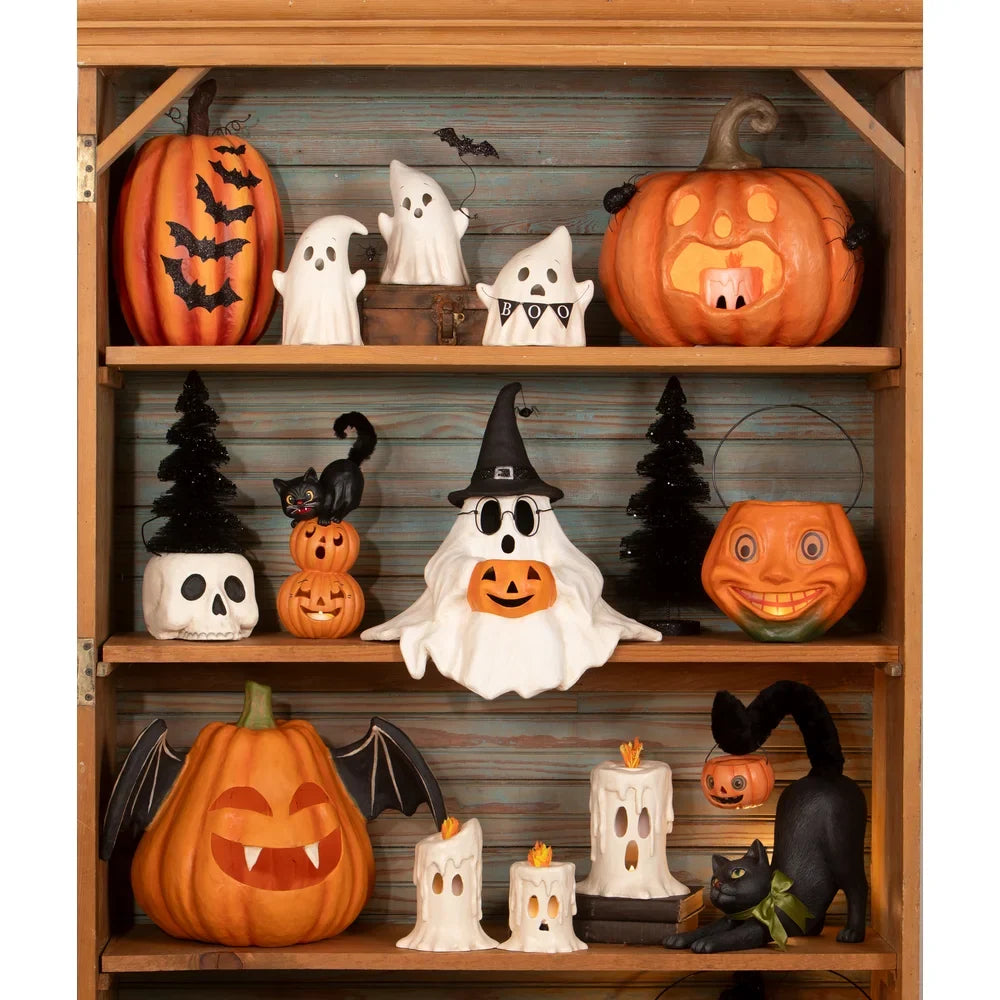 Bethany Lowe Designs - Frightened Fergus is a ghost with a sweet expression and glasses. He is wearing a witch hat with a spider dropping from it and holding a jack o lantern in his lap. He sits on a shelf amongst other Bethany Lowe vintage inspired Halloween characters. 